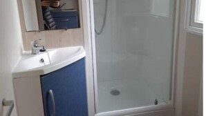 A bathroom with a glass-enclosed shower, a sink with a mirror above it, and a toilet. - Mobil-home C007 (Boofzheim)