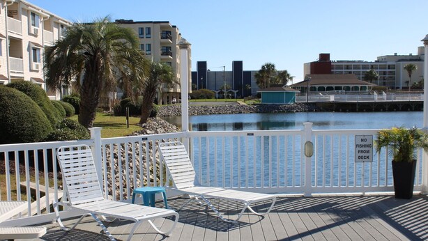 A deck with white metal chairs and a table, overlooking a body of water with a 'NO FISHING FROM DECK' sign.