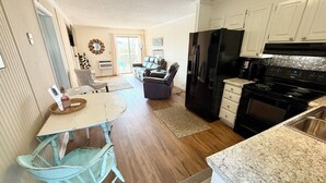 A kitchen with a black refrigerator, white cabinets, and a granite countertop. There is a dining area with a white table and blue chairs.