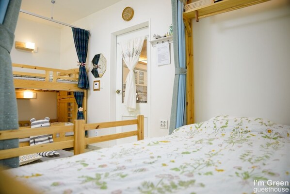 A room with bunk beds, a wooden headboard, a bed with a floral bedspread, a clock on the wall, and a window with curtains.