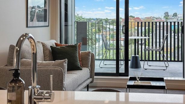 Una sala de estar moderna con un sofá, una mesita de centro y vistas a un balcón con mobiliario exterior.