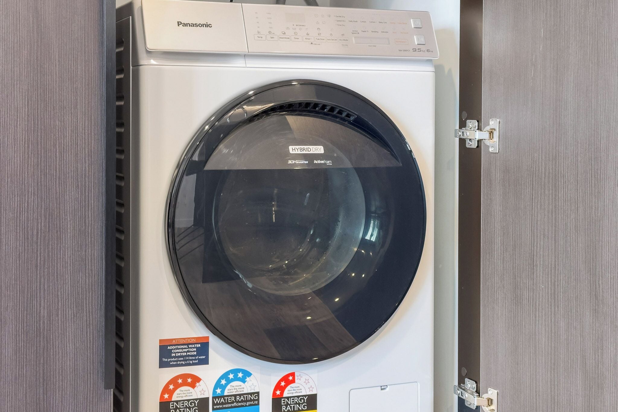 A front view of a white washing machine with a black door, labeled "HYBRID DRY."