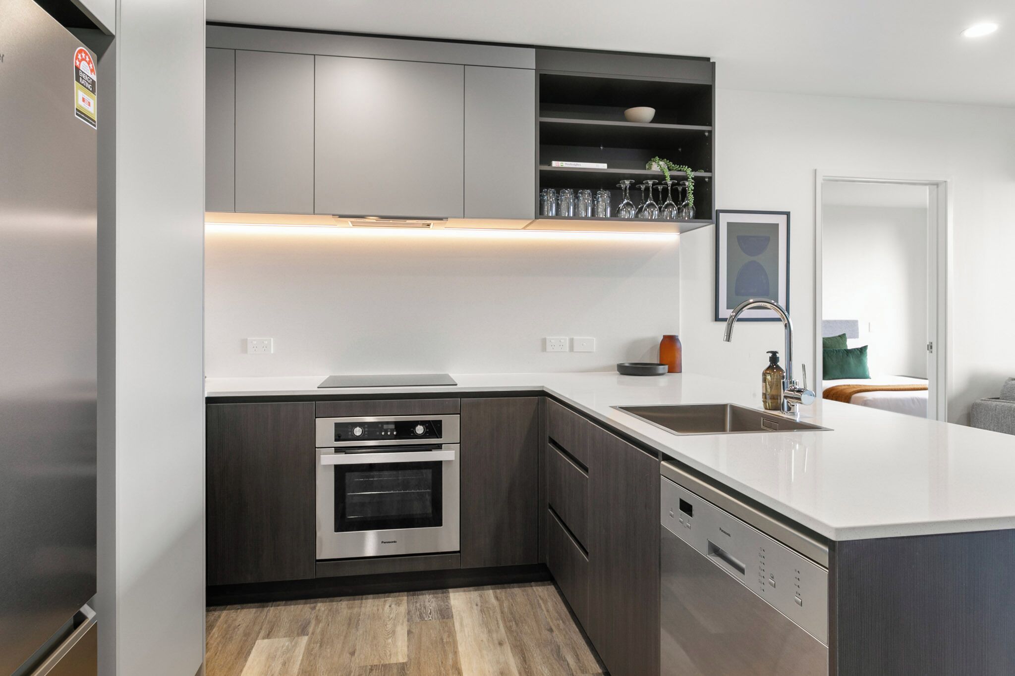 A modern kitchen with built-in appliances, a large island, and a view into a bedroom.