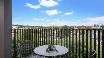 A balcony with a round table and two chairs, overlooking a residential area with houses and greenery.