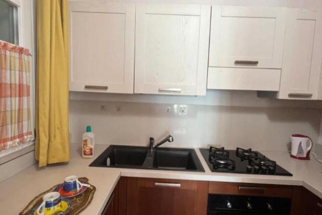 A kitchen with white cabinets, a black sink, a stove, and a kettle.
