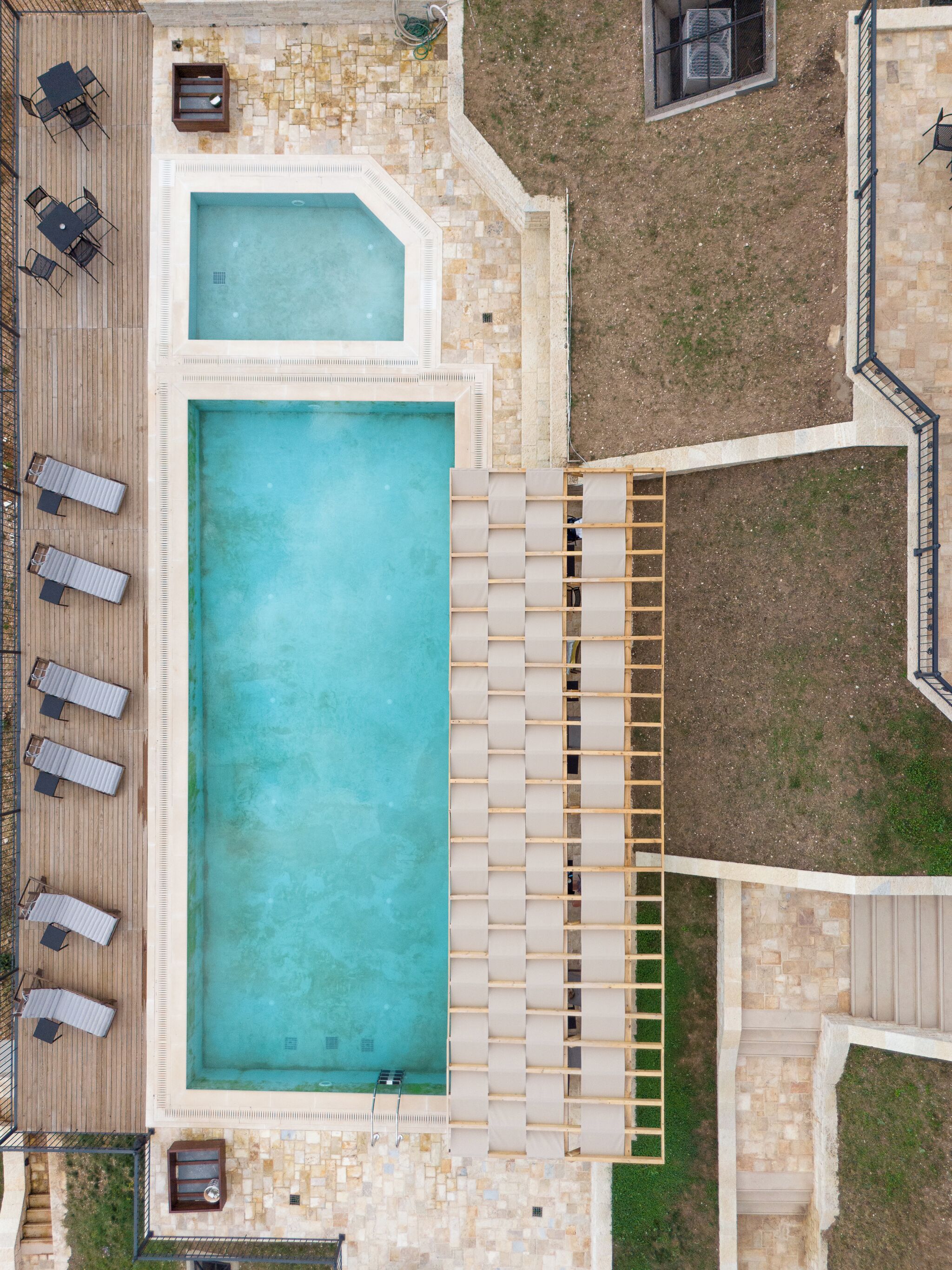 A rooftop pool with a wooden deck, lounge chairs, and a small garden area.