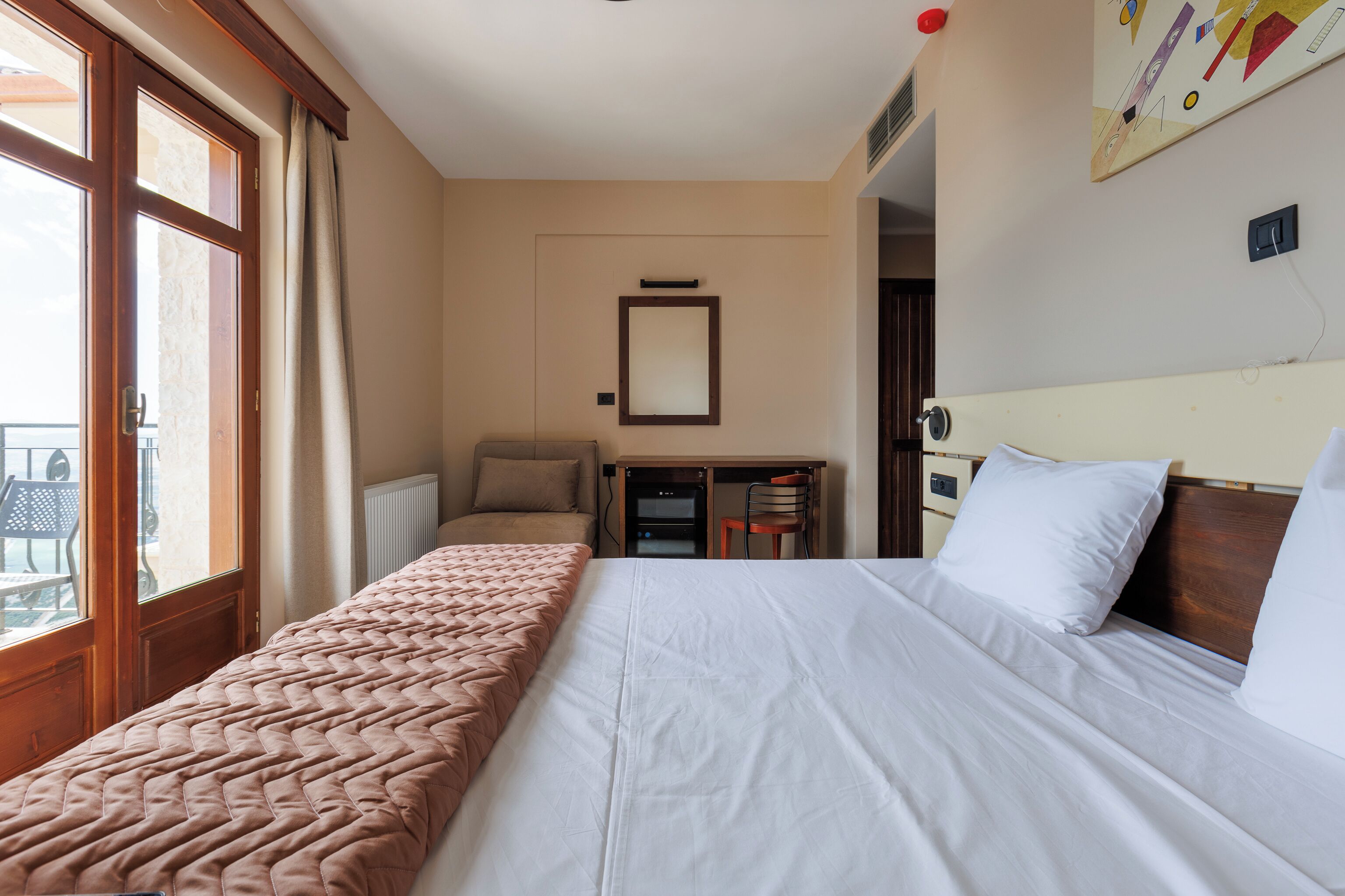 Ett hotellrum med en stor säng, ett skrivbord, en stol och ett fönster med gardiner.