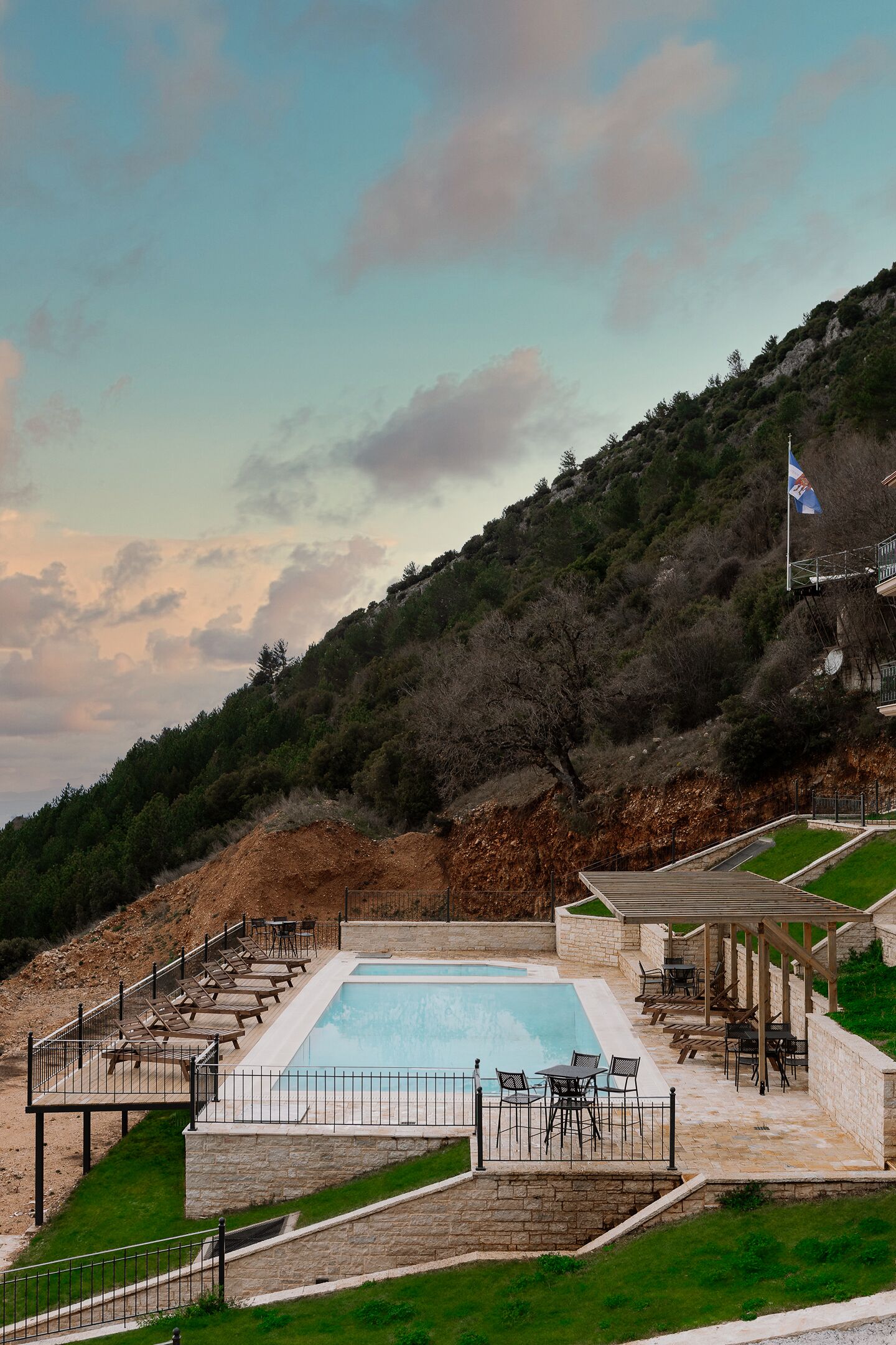 A pool area with a stone deck, lounge chairs, and a flag.