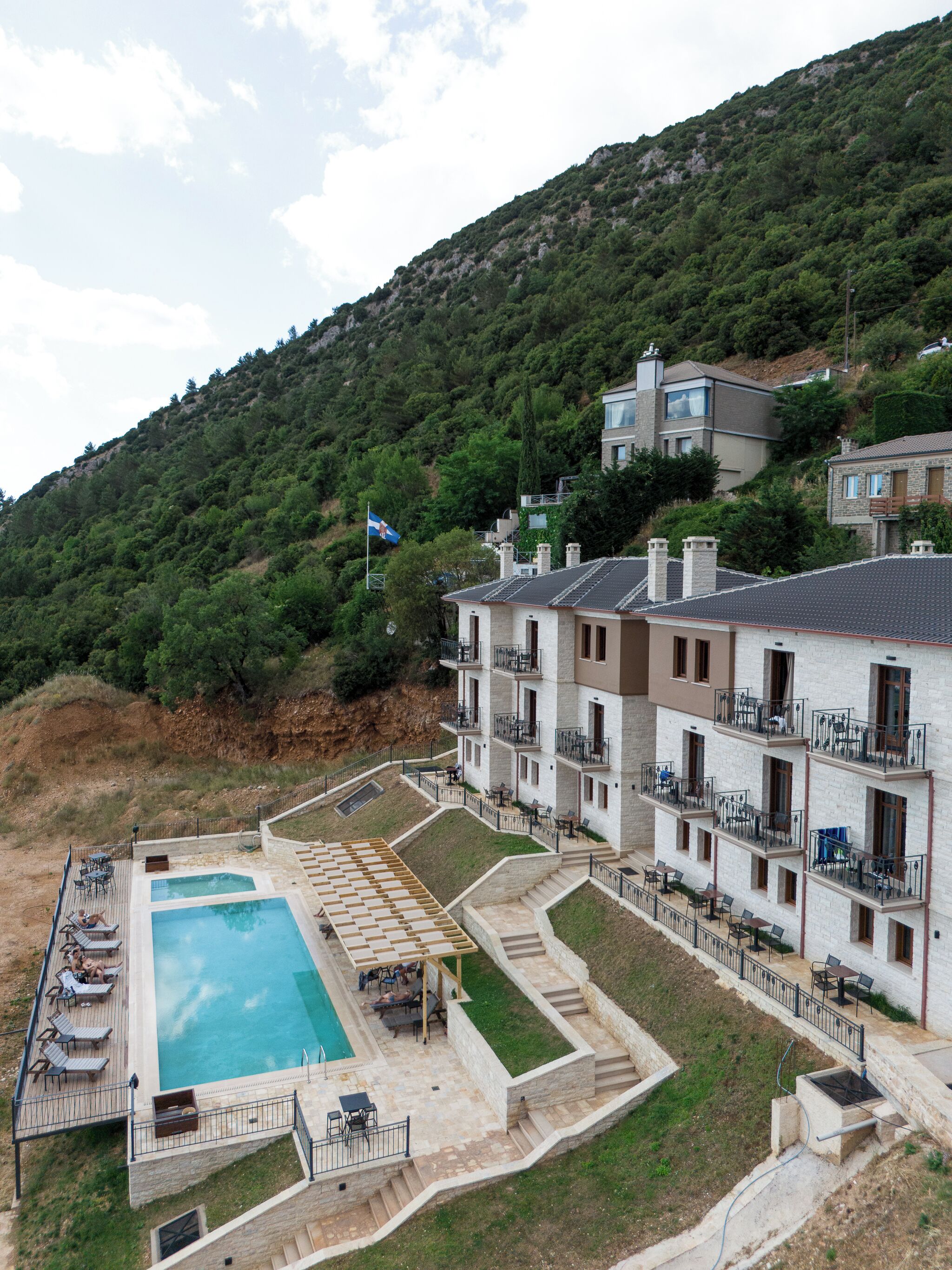 A residential building with multiple balconies, a swimming pool, and a hillside backdrop.