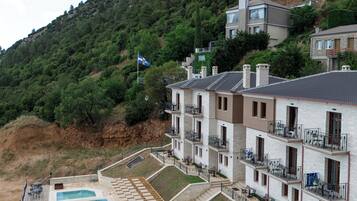 A residential building with multiple balconies, a swimming pool, and a hillside backdrop.