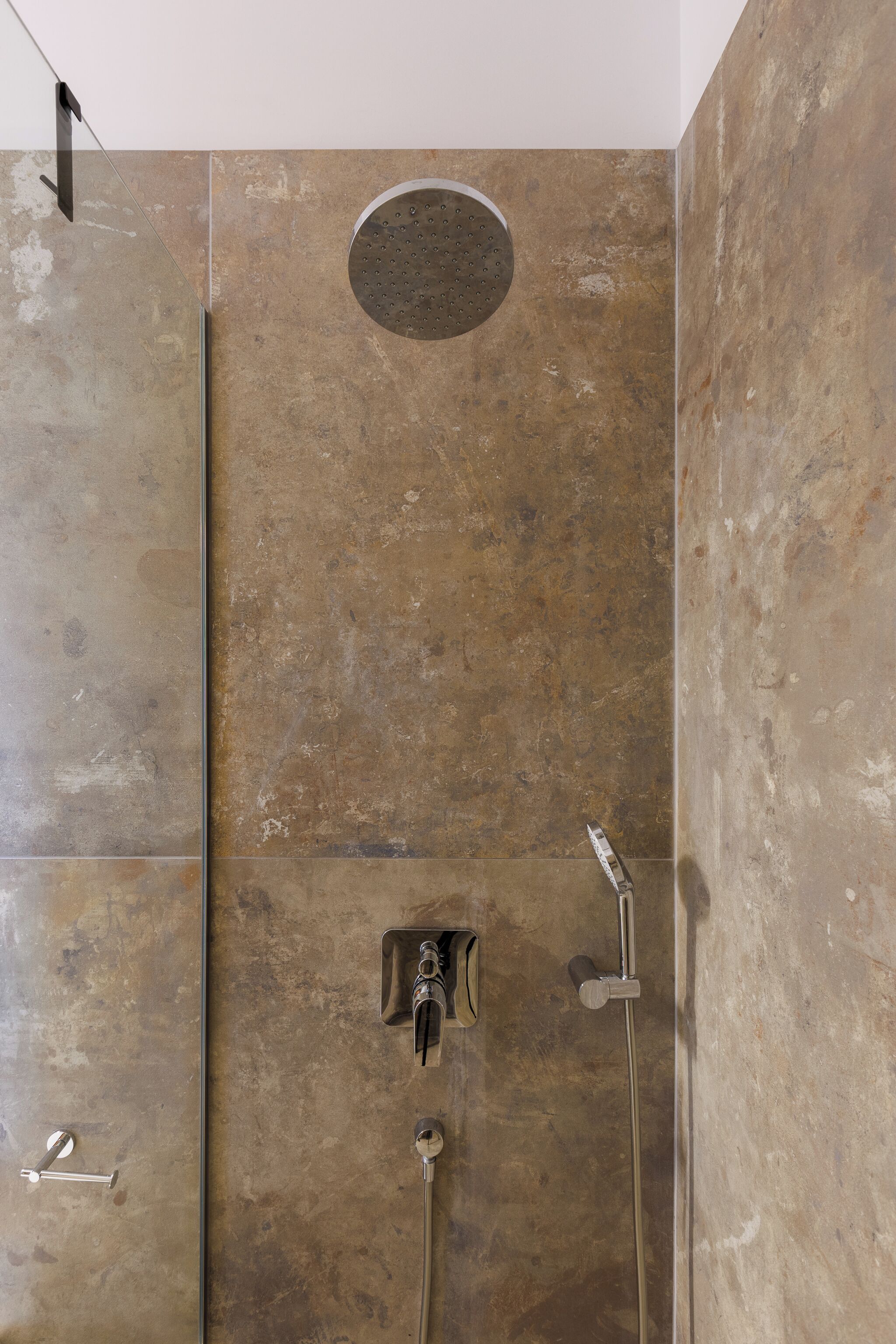 A shower with a circular rain showerhead and two handheld showerheads.