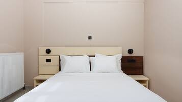 A neatly made bed in a hotel room with a simple headboard, two bedside tables, and a wall-mounted light fixture.