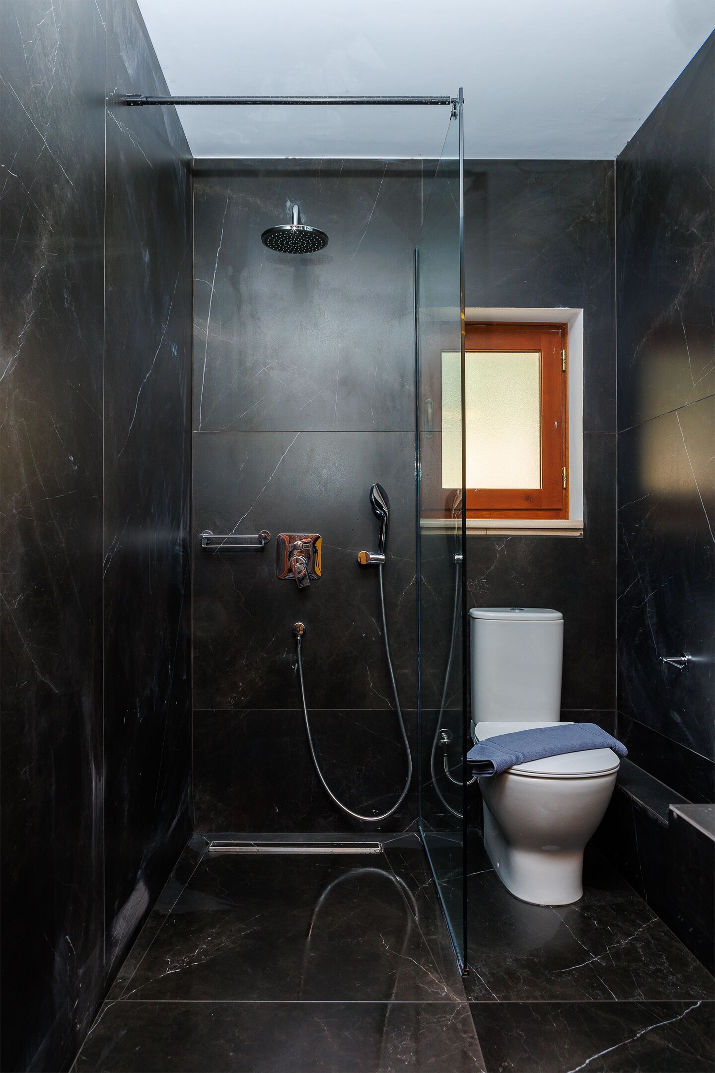 A modern bathroom with a glass-enclosed shower, a toilet, and a small window.