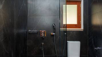 A modern bathroom with a glass-enclosed shower, a toilet, and a small window.