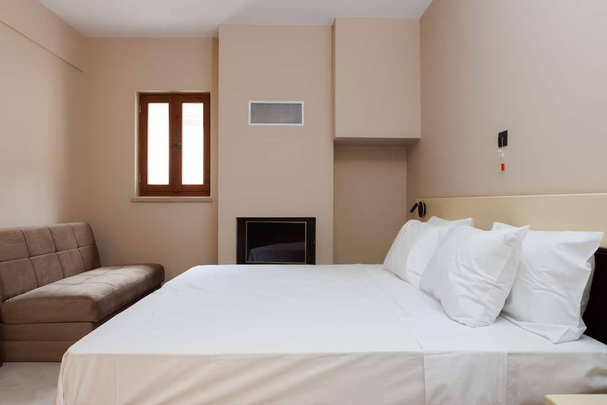 A hotel room with a bed, a sofa, a small TV, and a window.