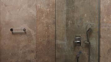 Une douche fermée par des parois en verre, dotée d’un pommeau de douche à main et d’un robinet mural.