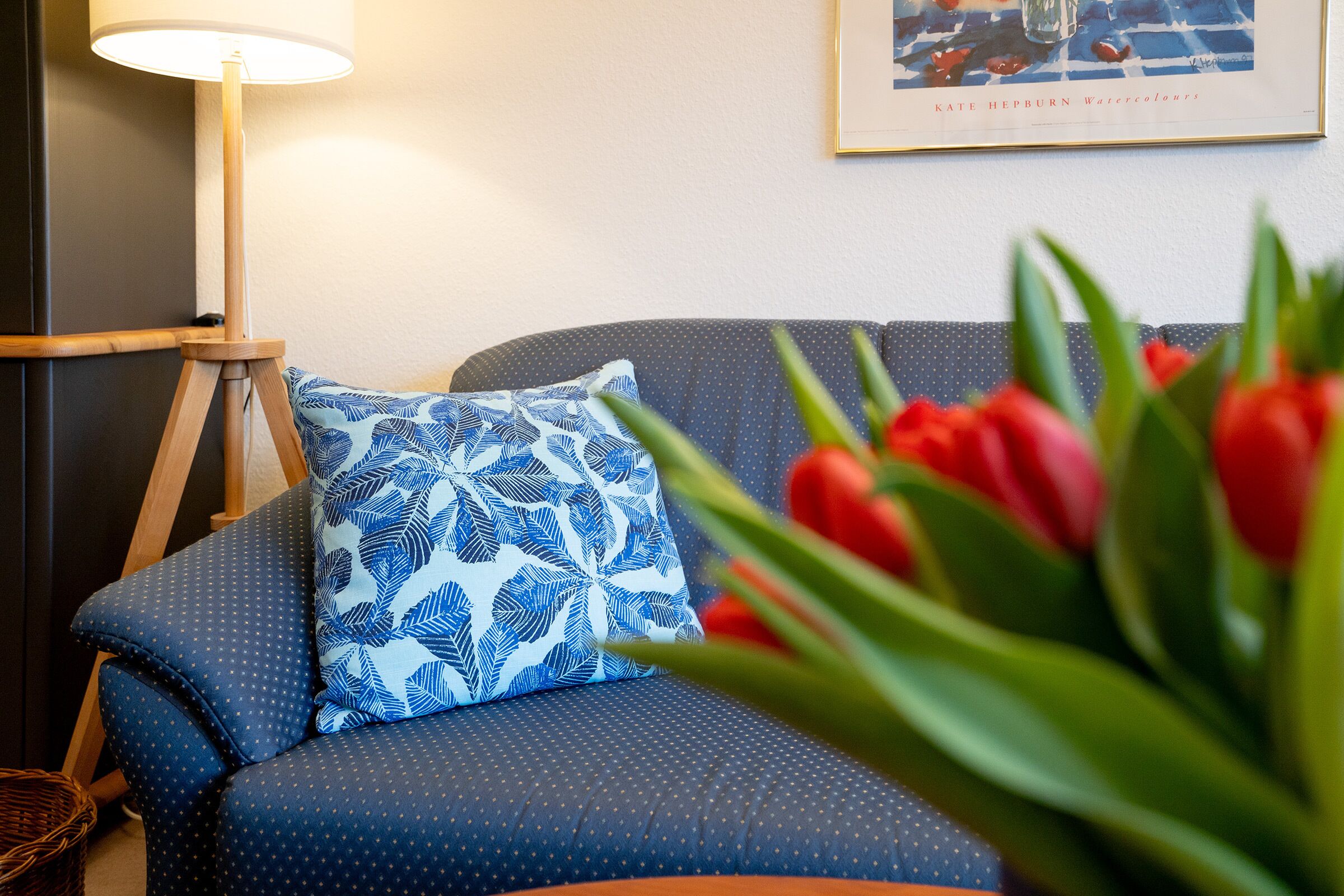 A room with a sofa, a patterned pillow, a lamp, and a framed artwork on the wall.
