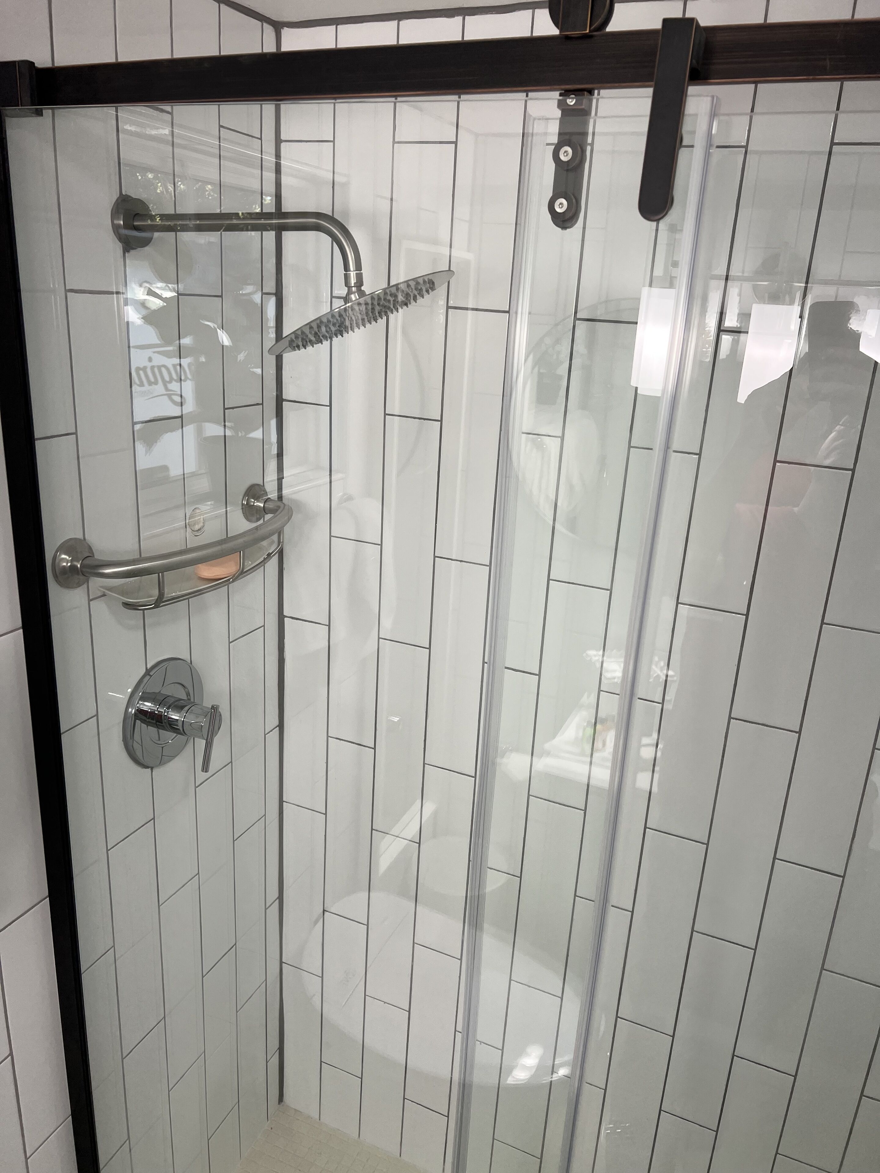 Une cabine de douche fermée par des parois en verre, équipée d’un pommeau de douche à main et d’un distributeur de savon à main.