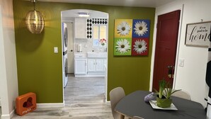 A modern kitchen with white cabinets, a red door, and a dining area with a table and chairs.