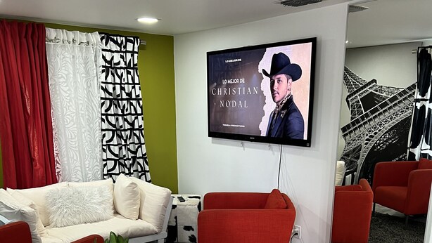 A modern living room with a sofa, red chairs, a dining table with a vase of flowers, and a TV displaying a movie poster.