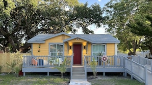 A yellow house with a red door, a front porch, and a small staircase leading to the entrance.