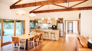 Une cuisine moderne avec des poutres en bois, un coin repas doté d’une grande table et de chaises, et un espace salon confortable avec un canapé.