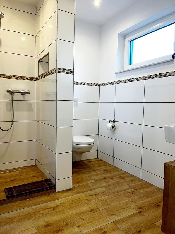 Une salle de bain avec des carreaux blancs, une douche, des toilettes et un plancher en bois.