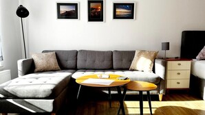 Un salon moderne avec un canapé d’angle, une table basse, une table d’appoint et trois tableaux encadrés accrochés au mur.