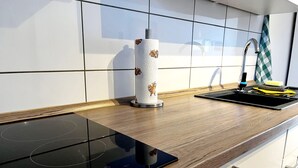 Une cuisine moderne avec une plaque de cuisson à induction noire, un porte-essuie-tout, un évier avec un savonnière jaune et un torchon à carreaux.