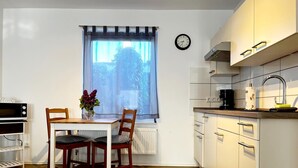 Une cuisine de taille réduite comprenant une table à manger, des chaises, une horloge et une fenêtre donnant sur un paysage agréable.