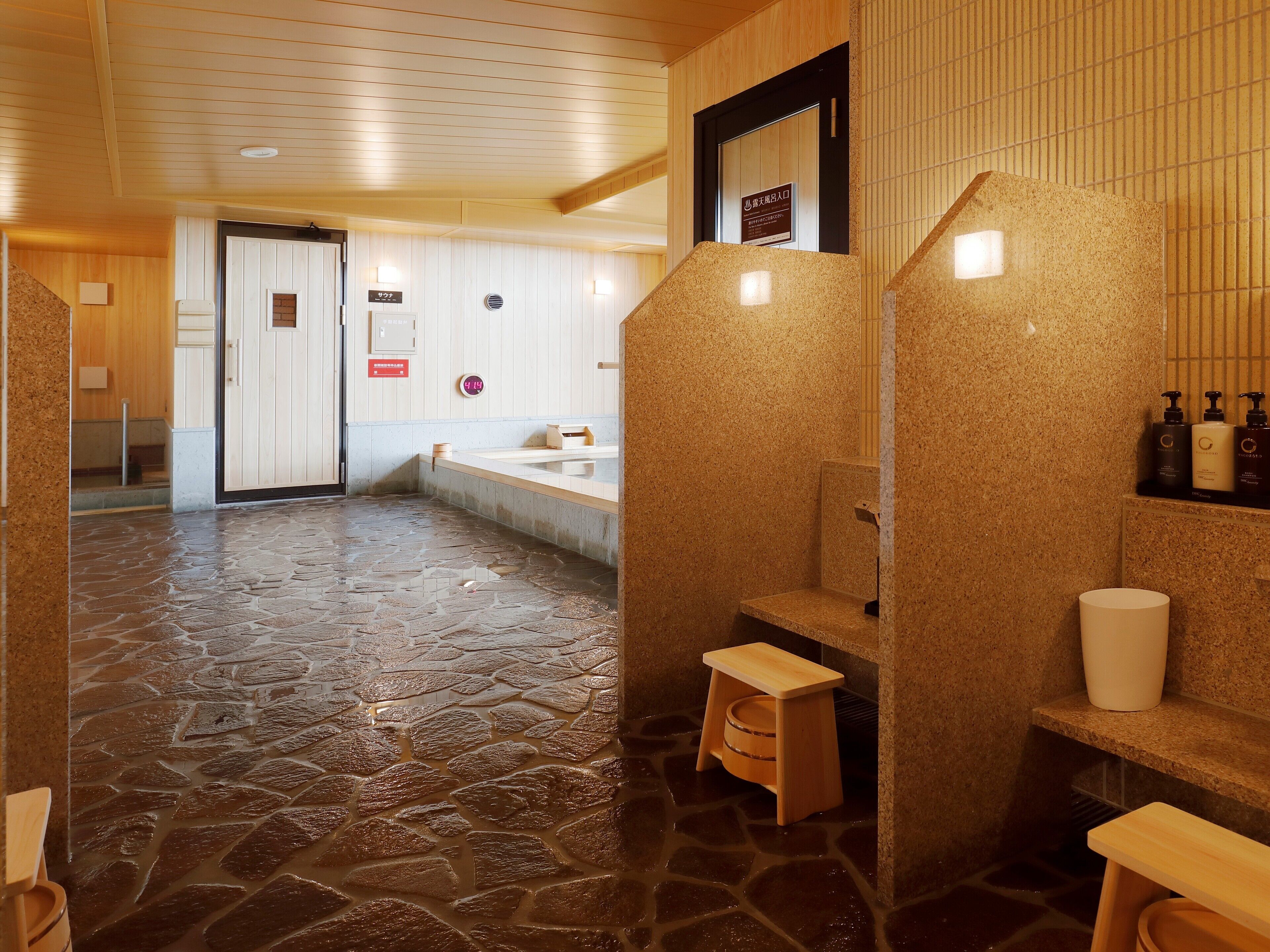 A stone-floored bathroom with a wooden bench, a sink, and toiletries on a shelf.
