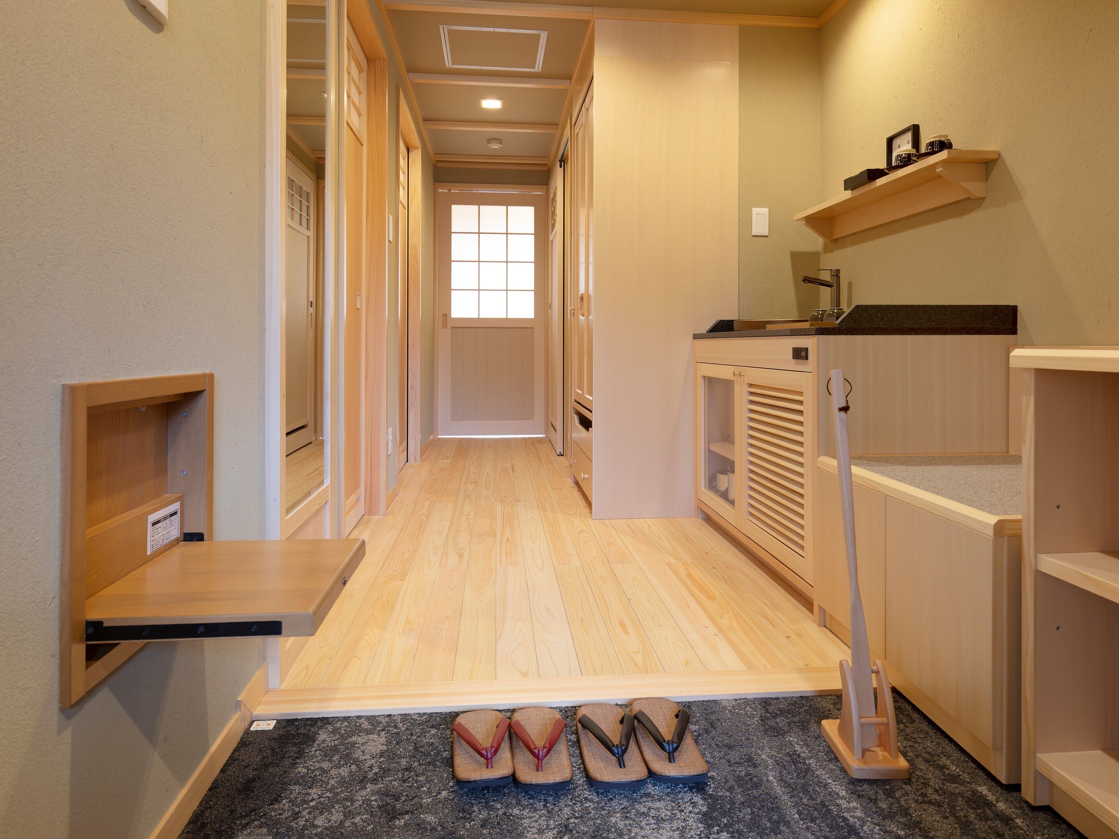 Un couloir doté d’un plancher en bois, d’un meuble à chaussures, d’une petite table et d’un meuble avec une porte en verre.