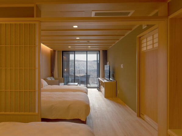 Habitación de hotel con dos camas, un escritorio, un televisor y un balcón al que se accede por una puerta corredera.