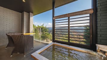 A balcony with a view of a mountainous landscape, a wooden table, and a wicker chair.