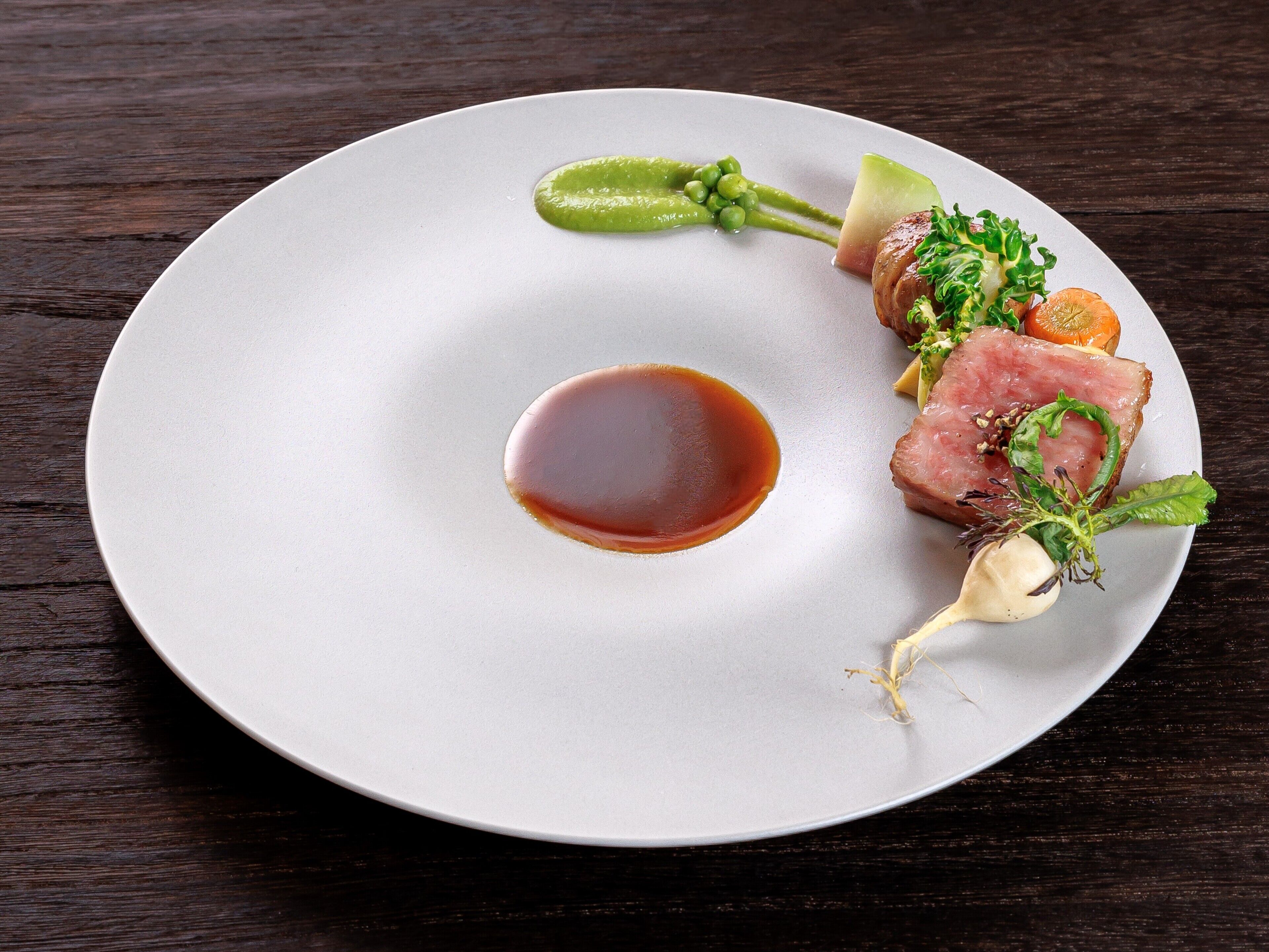 Une assiette blanche avec une quenelle de sauce au centre, entourée d’un plat joliment présenté, composé de viande, de légumes et d’une garniture.