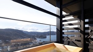 Un interior moderno con un ventanal grande con vistas a un paisaje pintoresco, un banco de madera y una barandilla metálica.