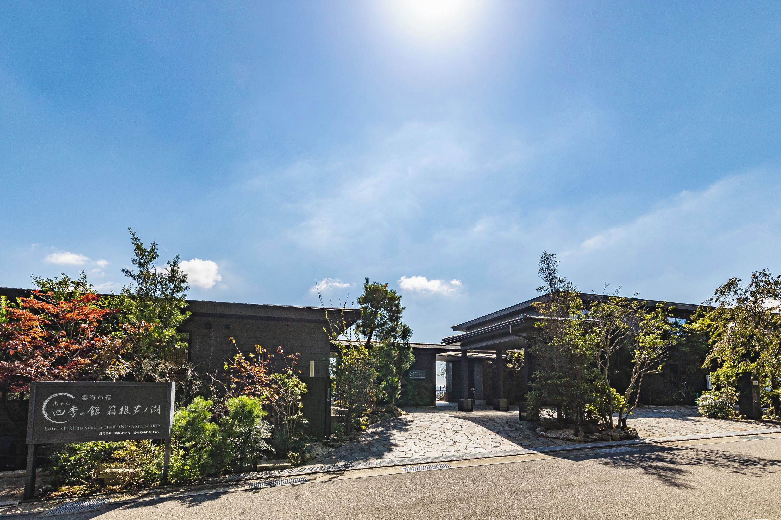 A hotel entrance with a stone pathway leading to a covered area, surrounded by various plants and trees.