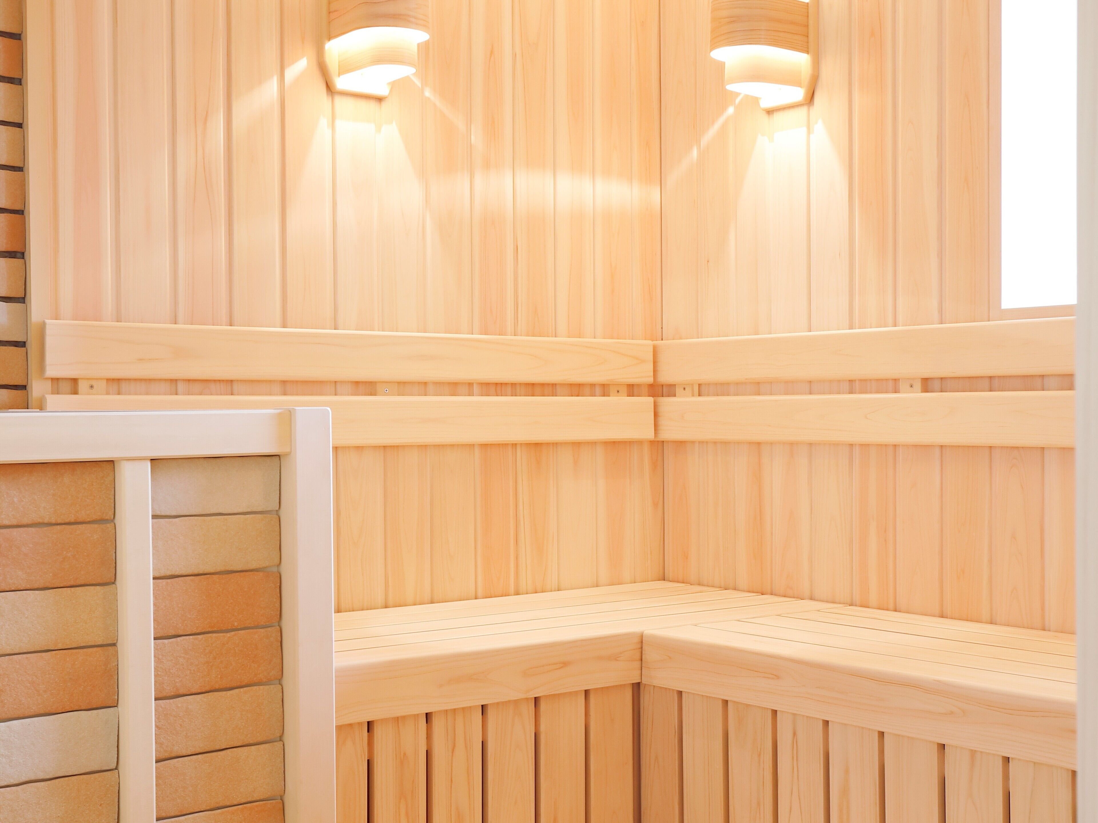 A sauna with wooden walls and benches, equipped with wall-mounted lighting.