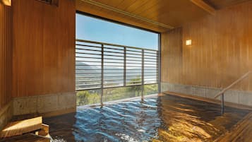 A wooden interior with a large window, a hot spring bath, and a view of a mountainous landscape.
