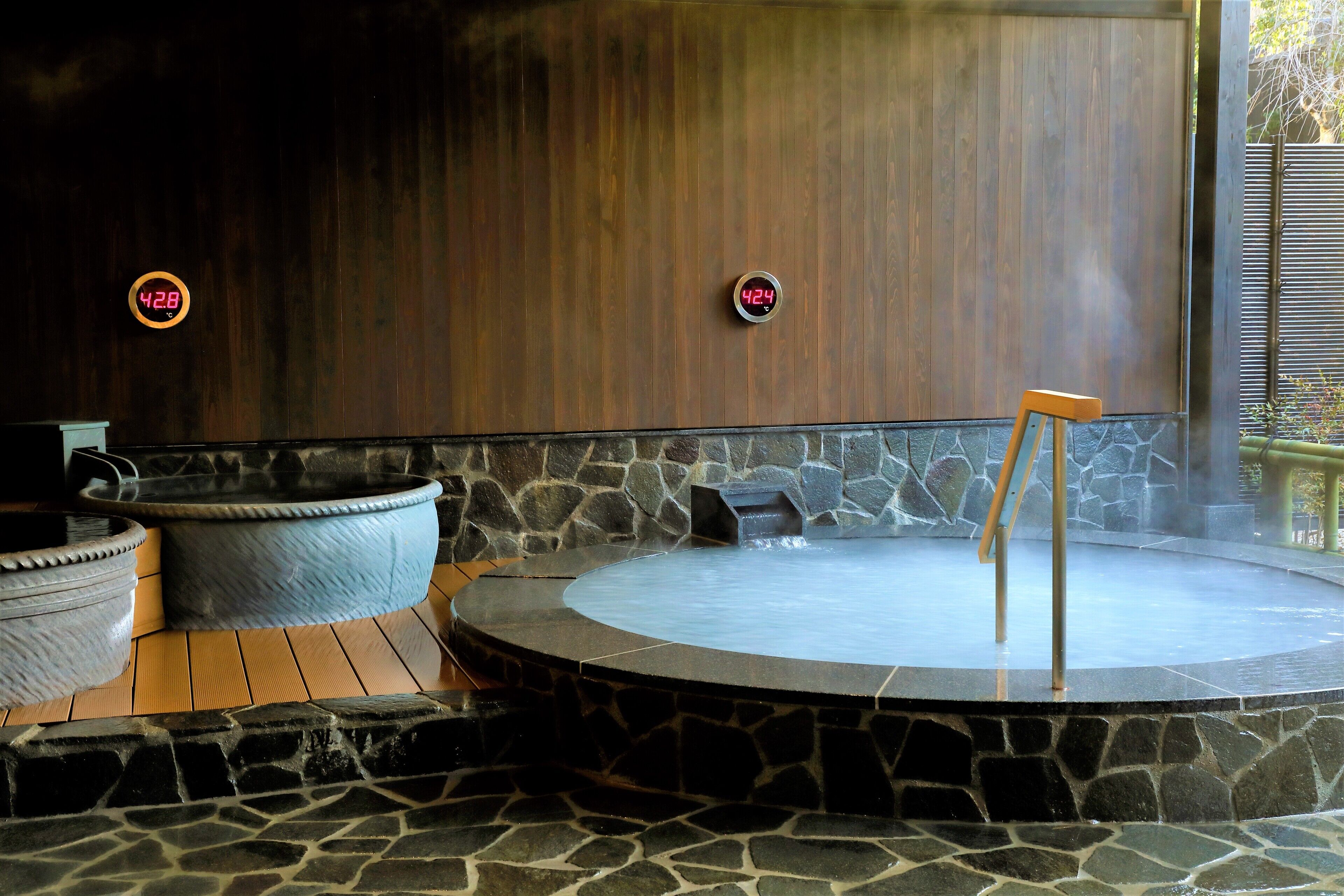 A hot tub area with stone flooring, wooden walls, and two digital thermometers.