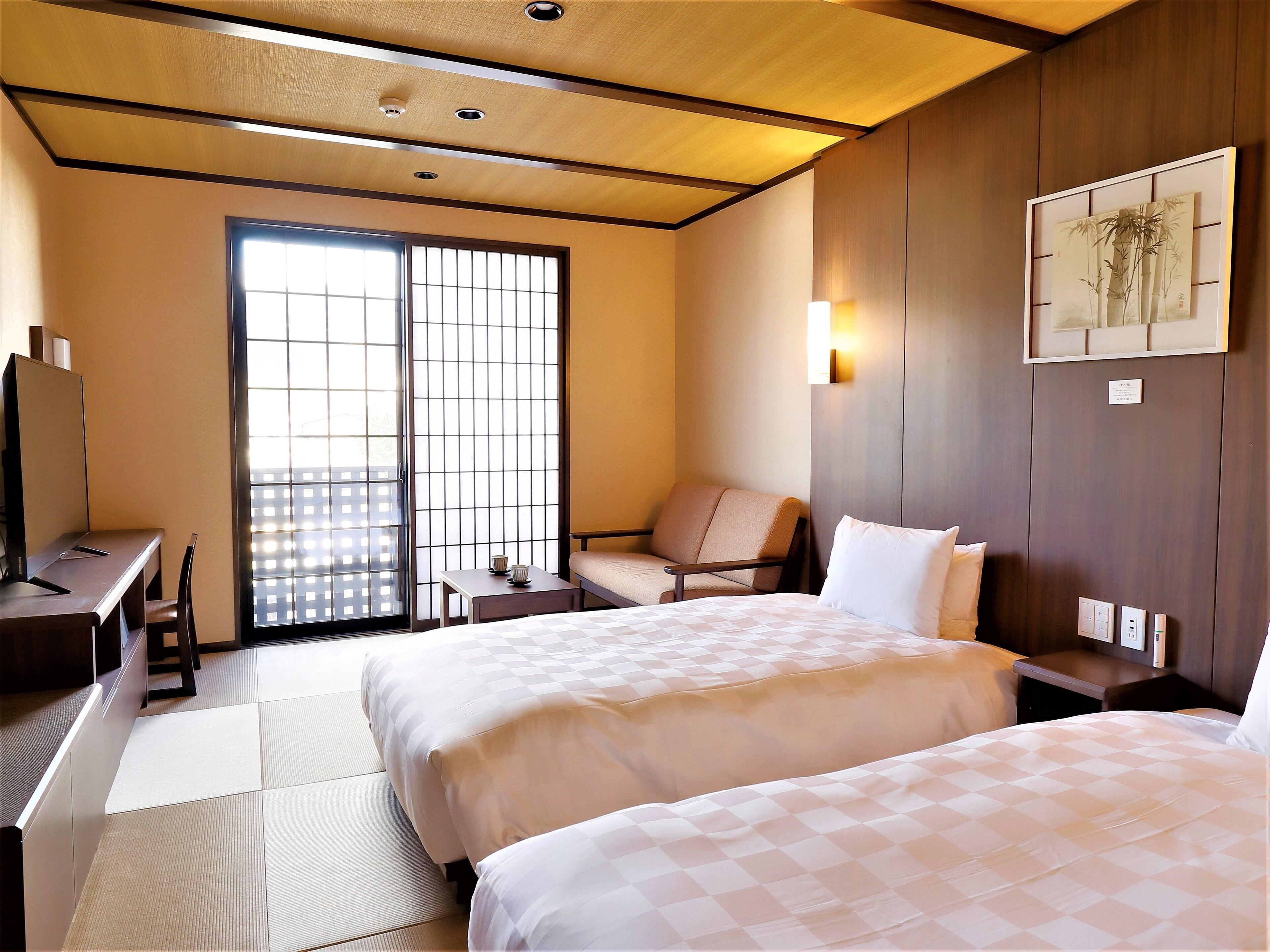 Habitación de hotel con dos camas, un escritorio, una silla y una puerta corredera al exterior.