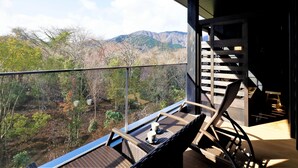 Ein Balkon mit Korbmöbeln, einer Glasreling und Blick auf Berge.