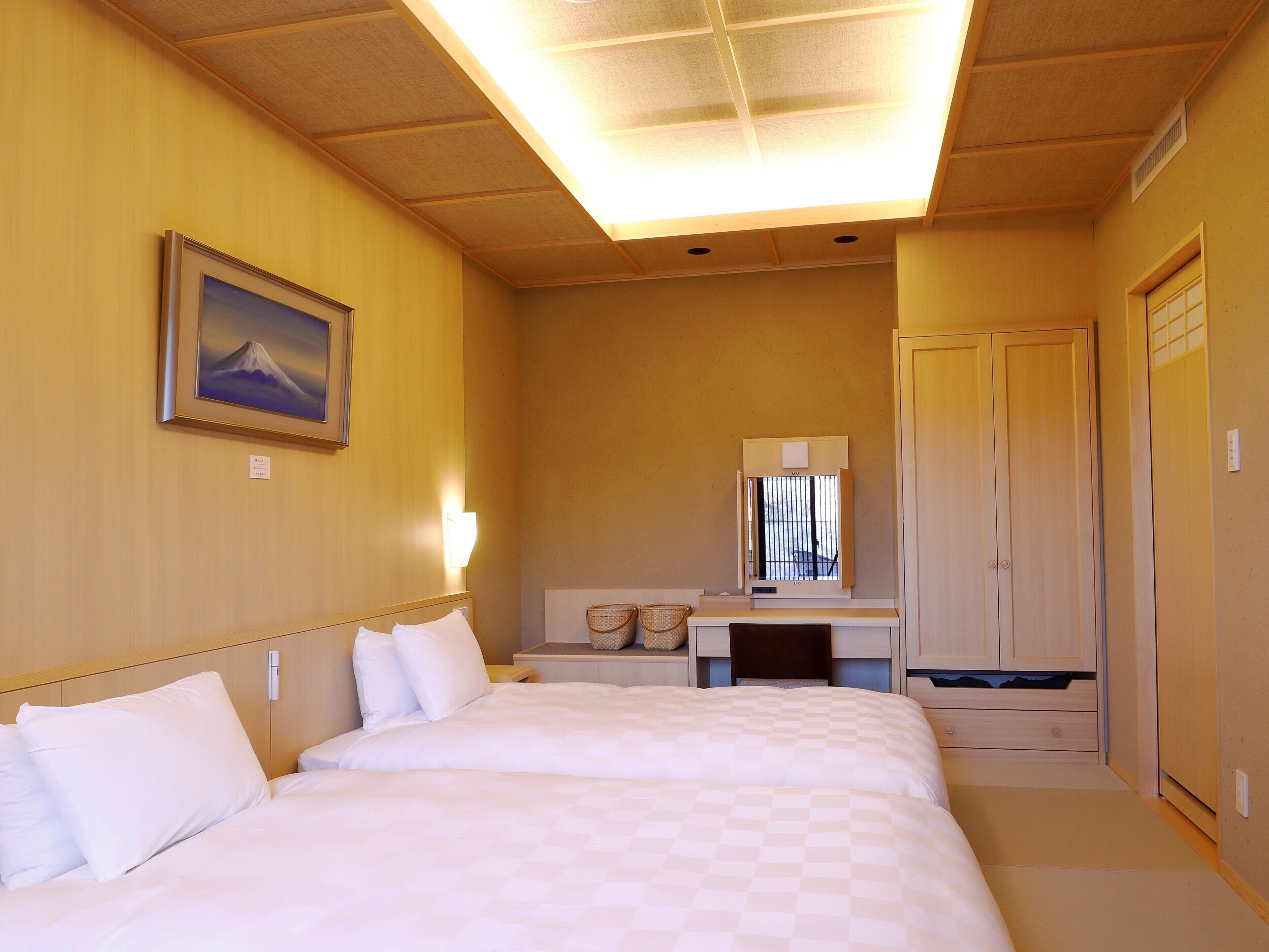 A hotel room with two beds, a desk with a mirror, a picture on the wall, and a wardrobe.