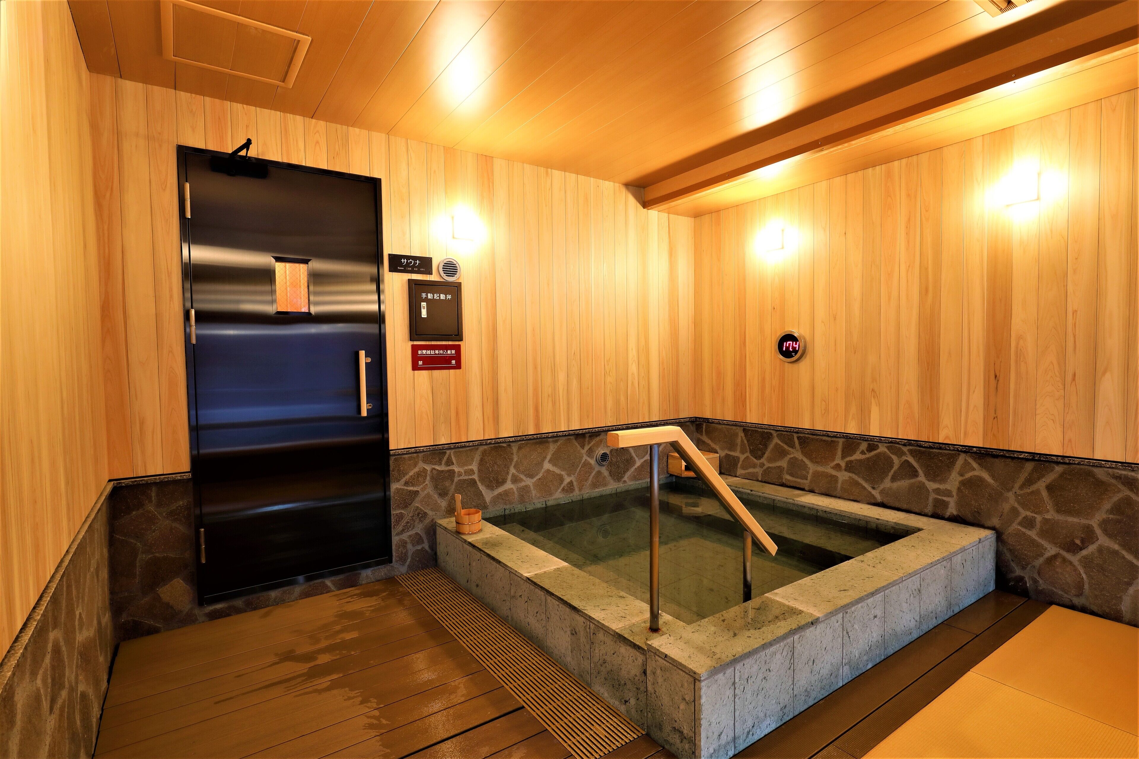 A sauna room with a stone wall, a wooden door, and a wooden floor.