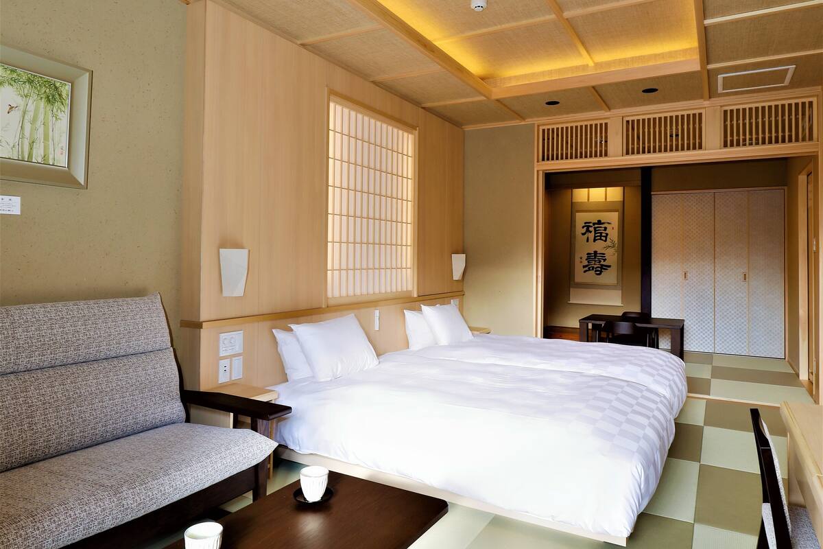 Hotellihuone, jossa on suuri sänky, sohva, pieni pöytä ja perinteinen liukuovi.