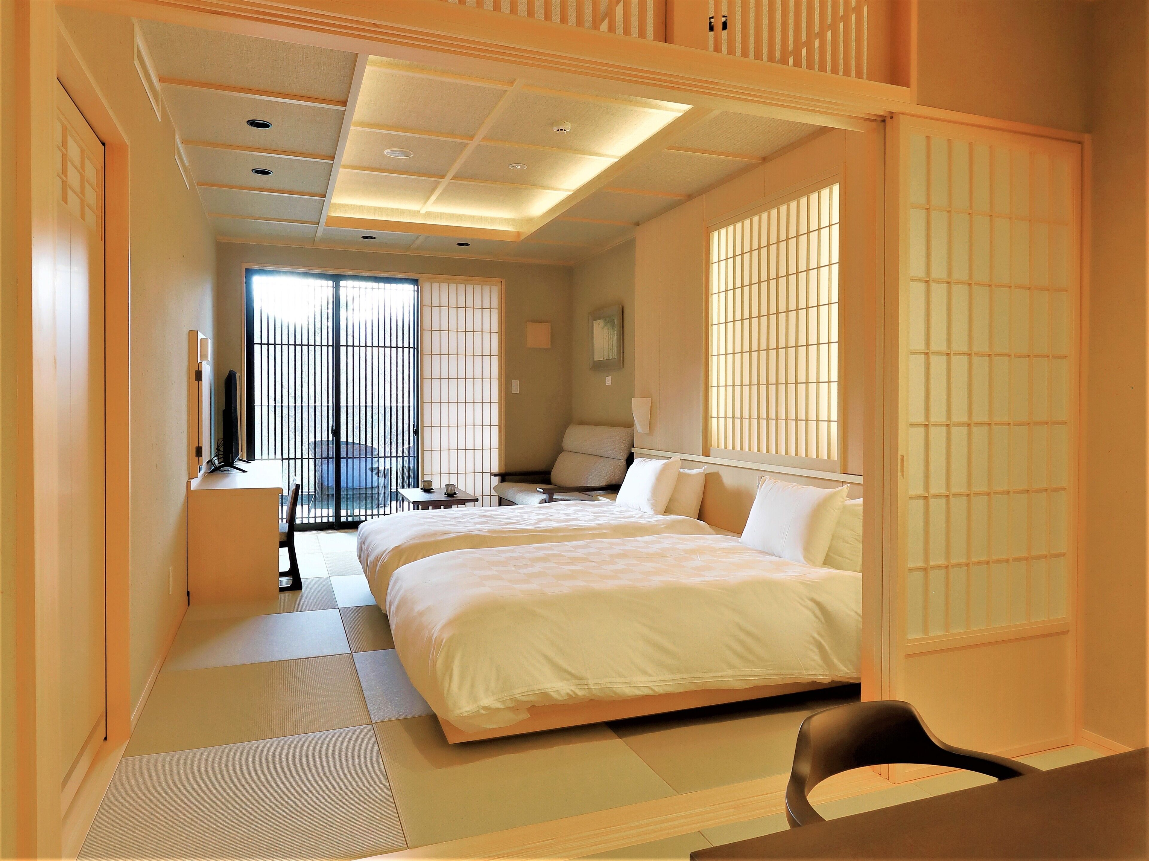 A hotel room with a large bed, a desk, a chair, and a view of the outside through a sliding door.