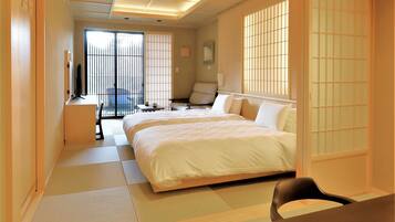 A hotel room with a large bed, a desk, a chair, and a view of the outside through a sliding door.