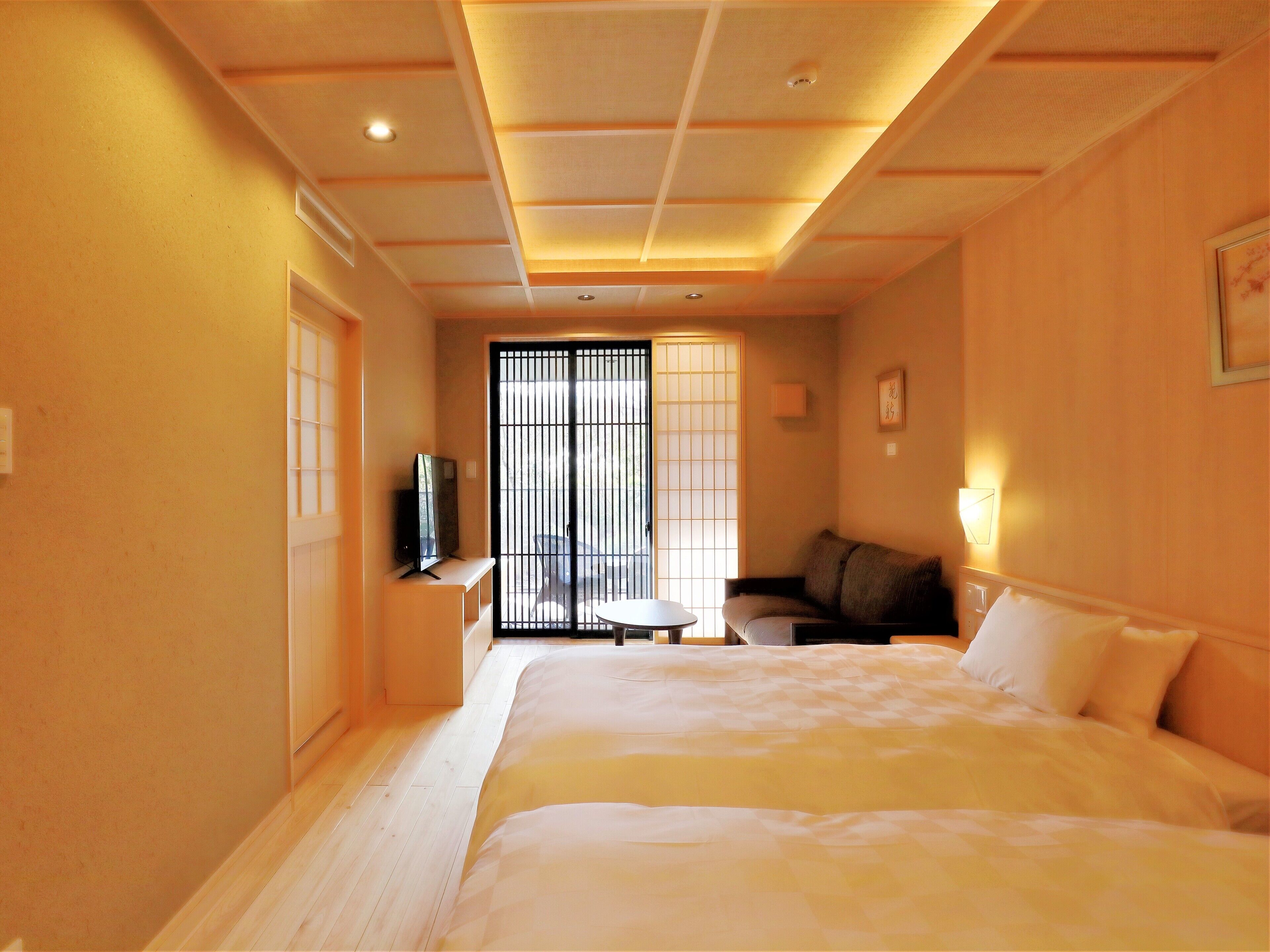 A hotel room with a large bed, a small table, a sofa, a TV, and a sliding door with a view.