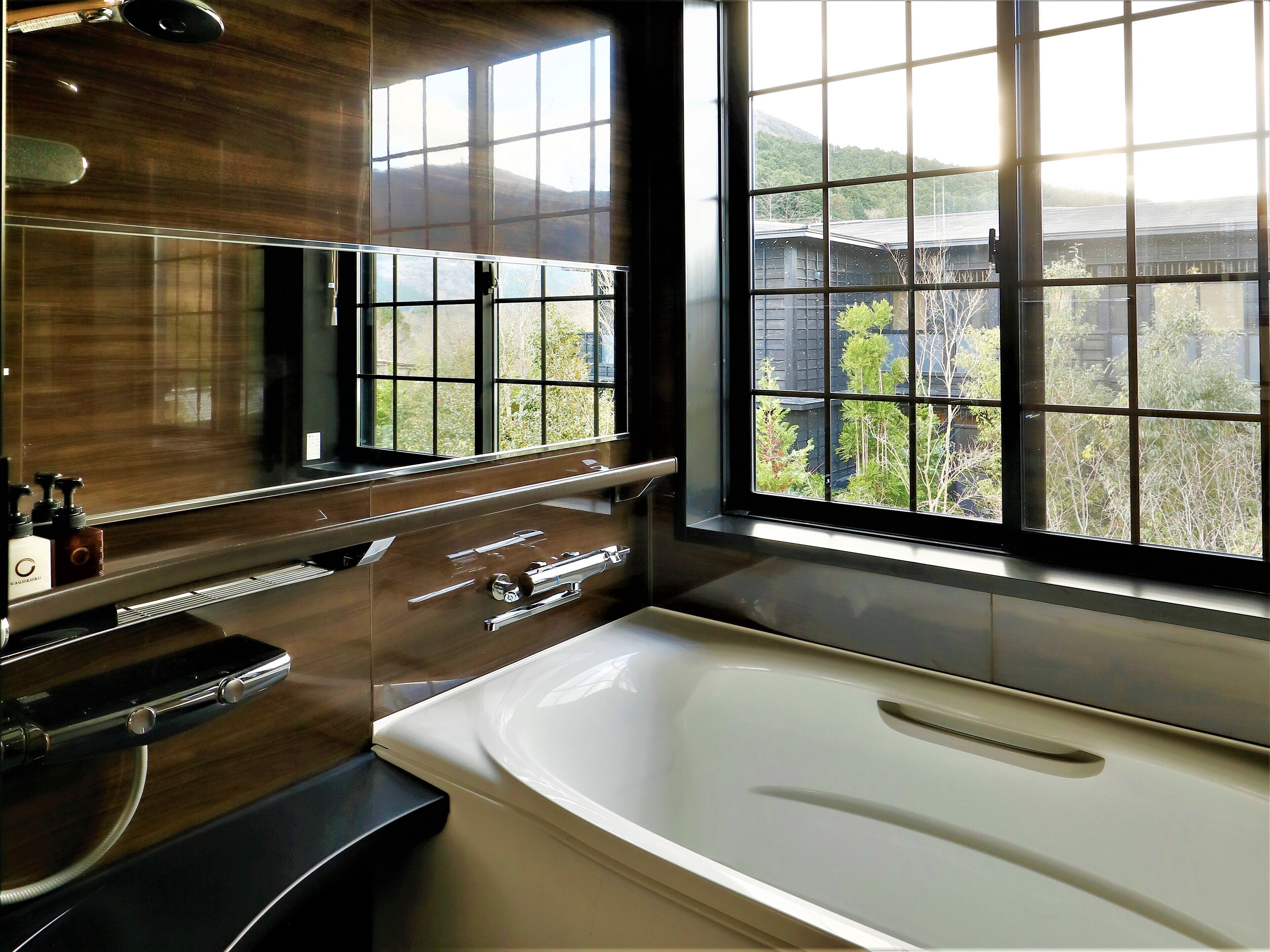 Ein modernes Badezimmer mit einer großen Badewanne, einem Spiegel und einem Fenster mit Blick auf Grünflächen und Gebäude.