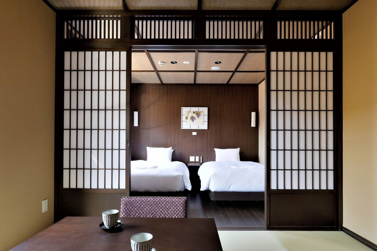 Perinteinen japanilaistyylinen huone, jossa on kaksi sänkyä, tatamimatosta tehty lattia ja matala pöytä sekä kaksi kuppia.